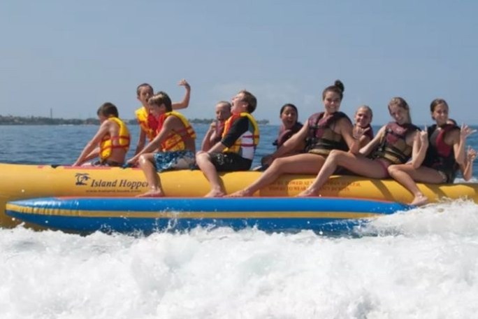 Group of people wearing life jackets riding a yellow banana boat on the ocean.