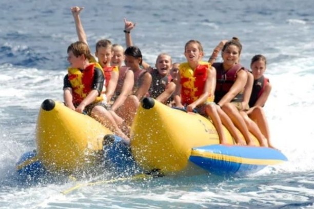 Group of people riding a banana boat on the ocean, wearing life jackets and smiling.