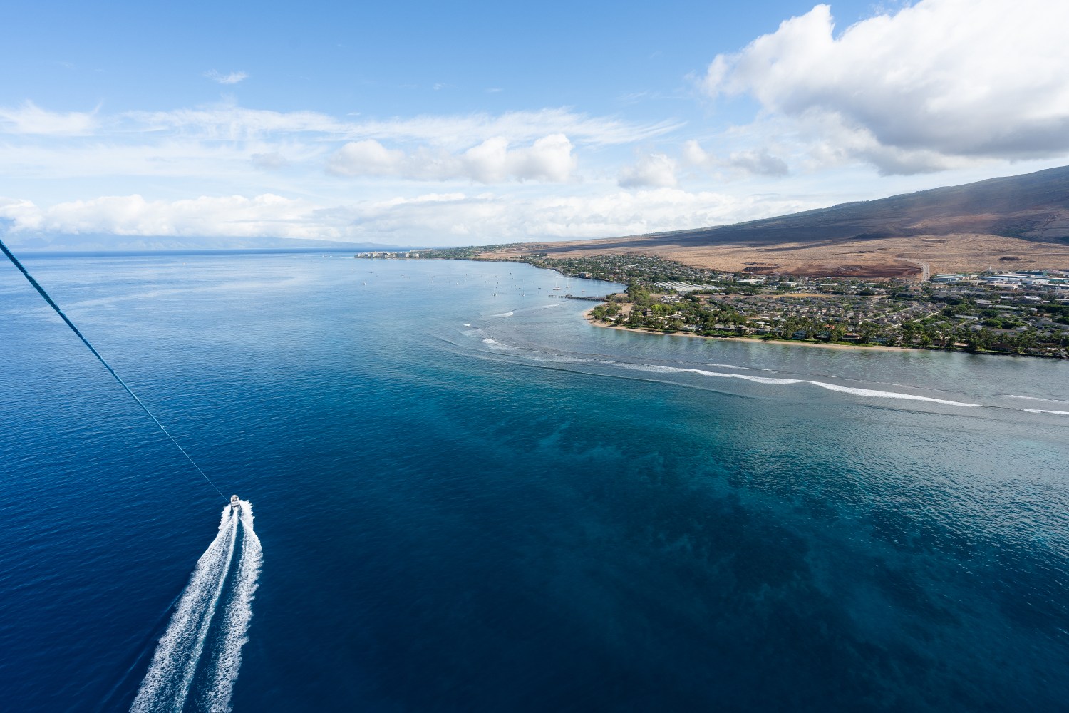 Aerial view of coastline and boat leaving wake in blue ocean under clear sky.