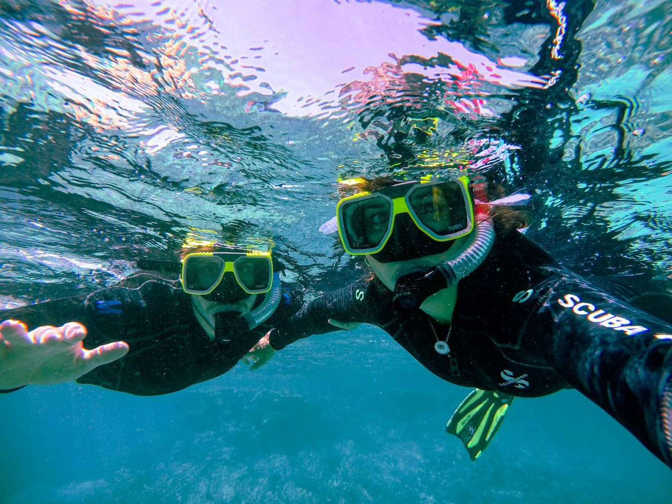 Two snorkelers underwater, wearing yellow masks and snorkeling gear, eyes visible.