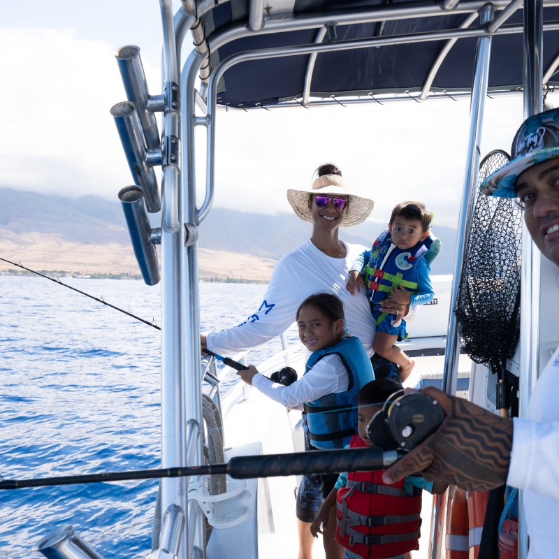 Family fishing on a boat with mountains in the background.