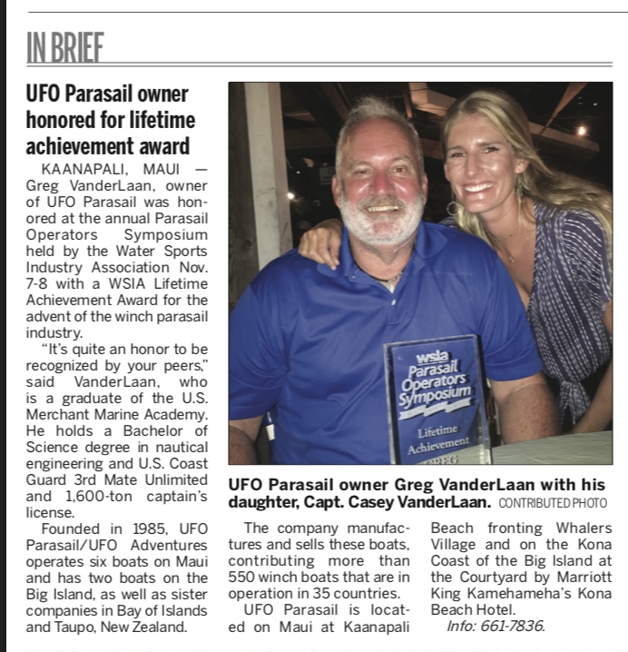 Man and woman smiling, holding an award plaque for lifetime achievement at a parasail operators symposium.