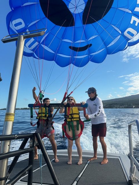 Two people parasailing with a blue parachute, guided by a person on a boat.