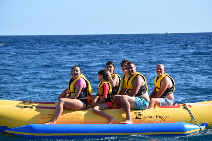 Group of people wearing life jackets on a banana boat in the ocean.