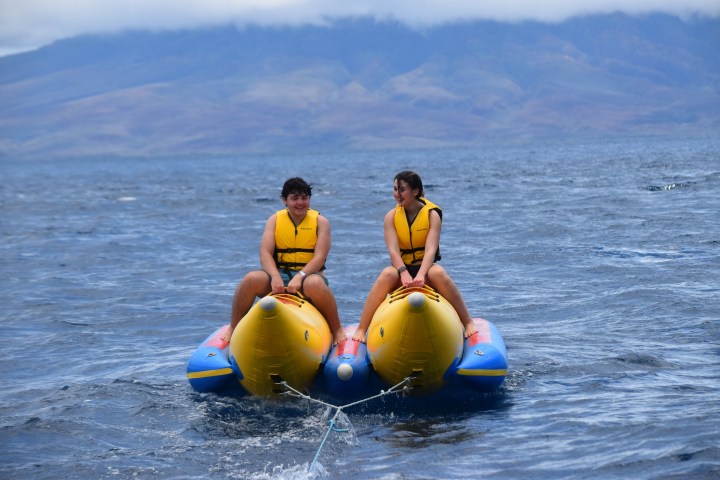 Two people on a yellow inflatable boat on the ocean, wearing yellow life jackets.