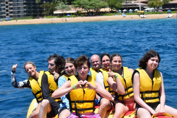 A group of people in yellow life jackets on a boat with ocean and beach in the background.
