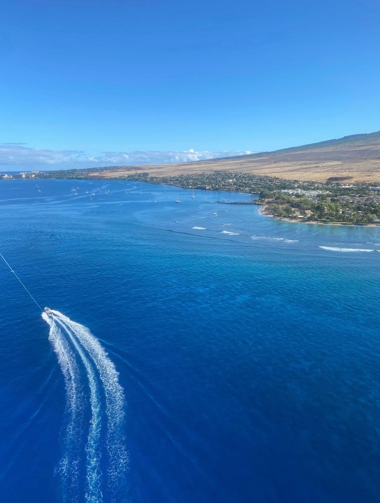 Aerial view of a boat creating a white wake on blue ocean near a coastline.
