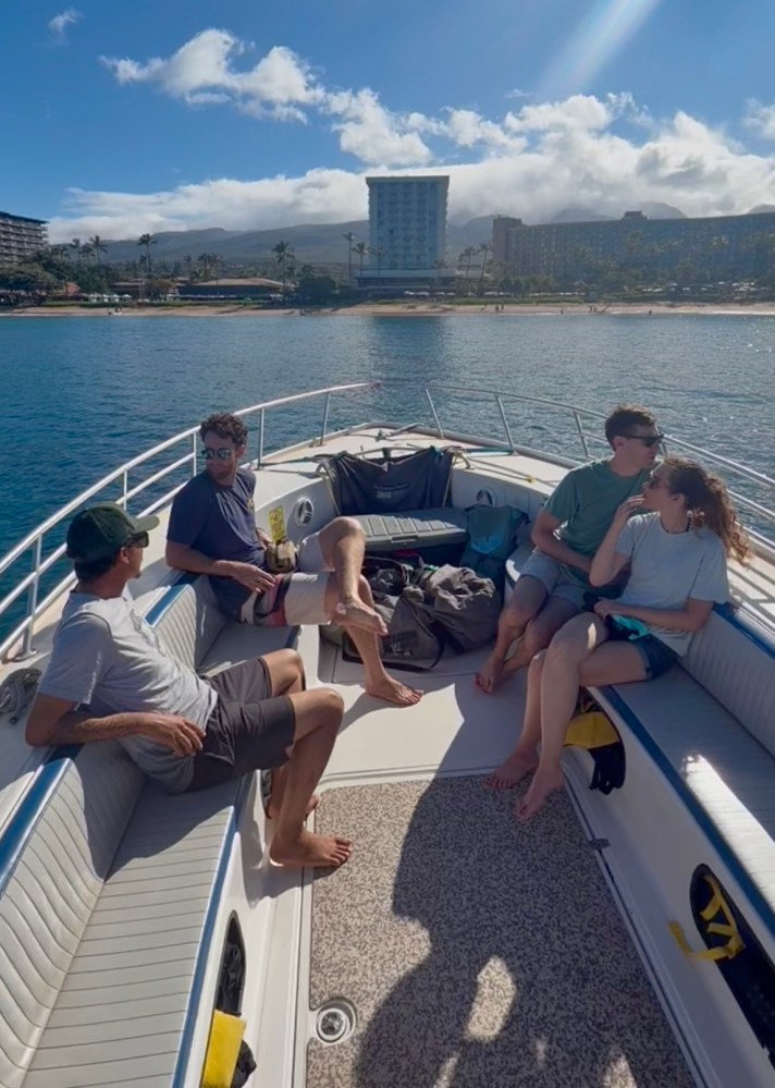 Four people sitting on a boat in sunny weather with cityscape in the background.
